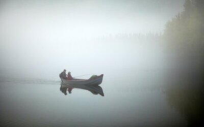 To personer i en liten båt med påhengsmotor kjører med fiskestang på en elv i tykk tåke